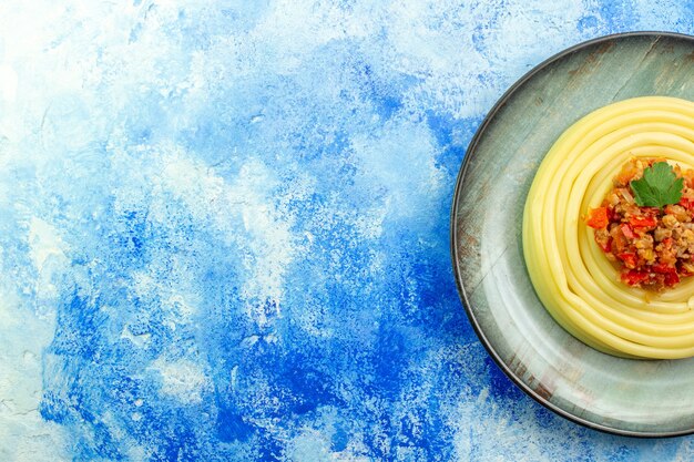 Overhead view of dinner with delicious spagetti on a gray plate on the left side on blue background