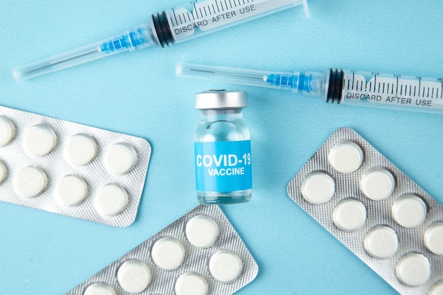 Free photo overhead view of disposable syringes and packed pills covid- vaccine ampoule on blue background