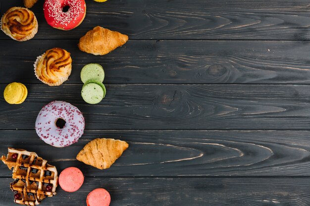 Free photo an overhead view of donut; macaroons; croissants; cupcake and waffles on wooden backdrop