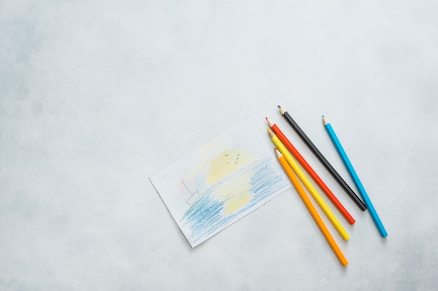 Overhead view of drawn paper and color pencils on white background