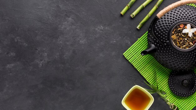 Вид сверху сушеной травы и бамбуковой палочки с чайником на черном фоне