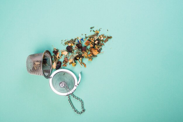 An overhead view of dried herbal tea with strainers on blue background