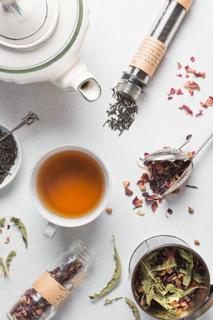 An overhead view of dried herbs with cup of tea and teapot on white background