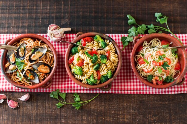 An overhead view of earthenware with different type of pasta on tablecloth