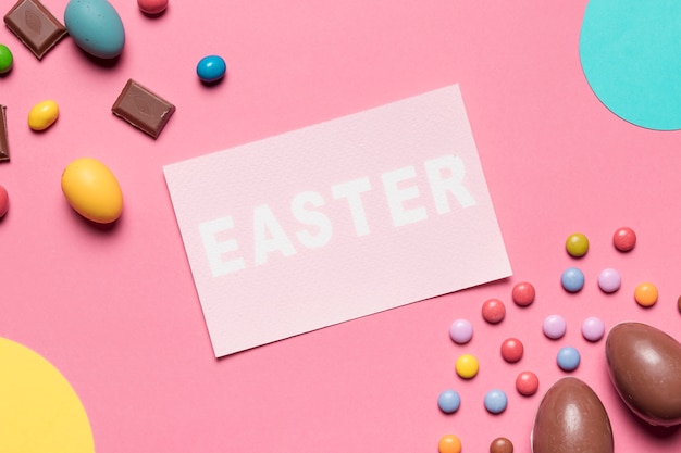 Foto gratuita una vista ambientale della parola di pasqua con le uova di pasqua del cioccolato e le caramelle della gemma su fondo rosa