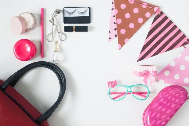 Overhead view of essential beauty items, Top view of party accessories, red hand bag, fashion eyeglasses and cosmetics, top view isolated on white background