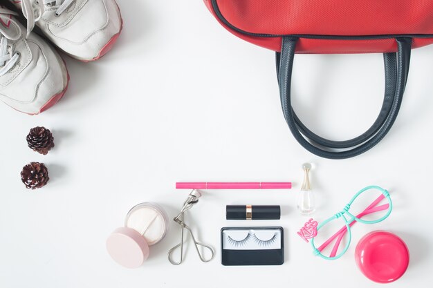 Overhead view of essential beauty items, Top view of red hand bag, fashion eyeglasses, cosmetics and sneakers, top view isolated on white background