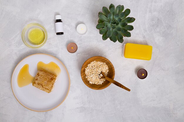 An overhead view of essential oil bottles; oats; cactus plant; yellow soap and honeycomb on concrete background