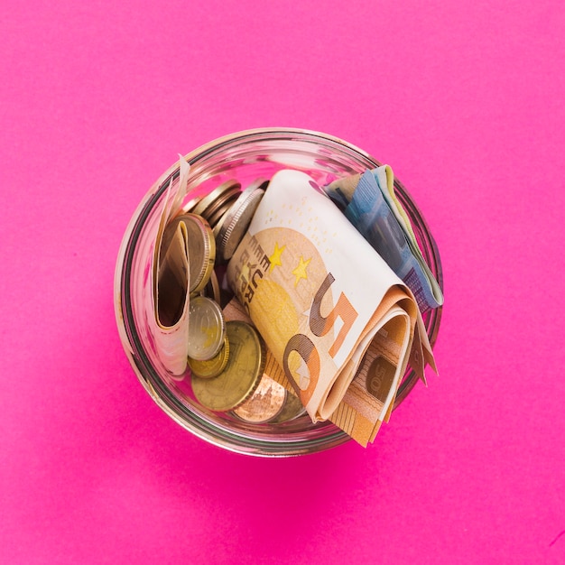 Foto gratuita una vista aerea di euro banconote e monete in vaso di vetro aperto su sfondo rosa