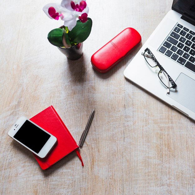 Верхний вид очков на ноутбуке с канцелярскими принадлежностями и сотовый телефон на столе