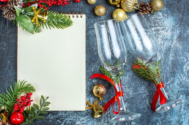 Overhead view of fallen glass goblets with red ribbon and decoration accessories next to notebook on dark background