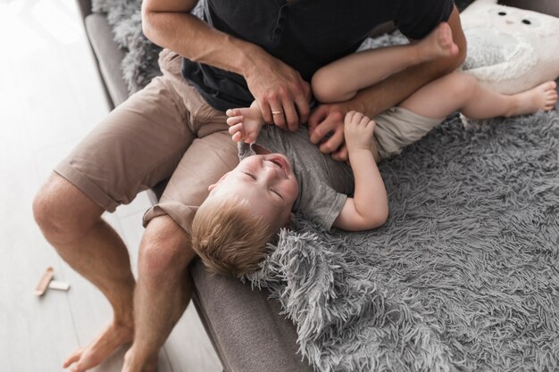 An overhead view of father sitting on sofa tickling her son