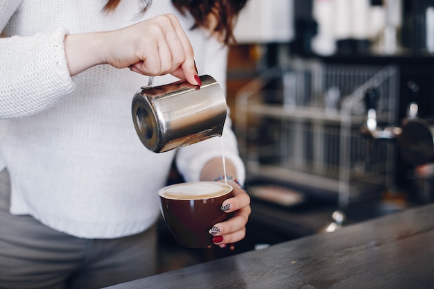 Overhead view female barista pouring milk foam into cappuchino in cafe