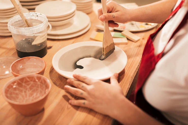 Free Photo an overhead view of female craftswoman painting the plate with paintbrush