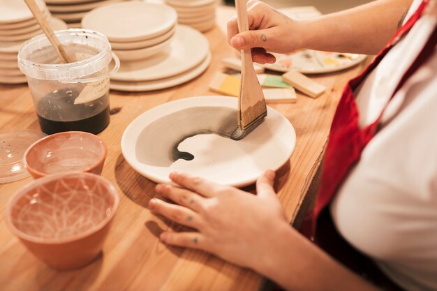 An overhead view of female craftswoman painting the plate with paintbrush