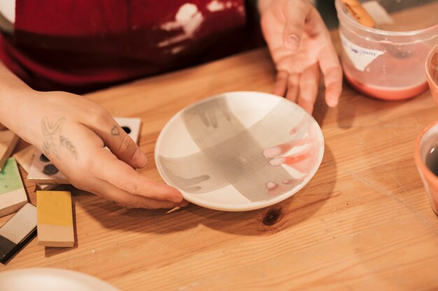 Вид сверху женского гончарного декоратора, держащего расписную керамическую тарелку