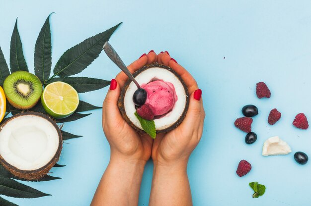 An overhead view of a female's hand holding coconut with frozen ice cream against blue background