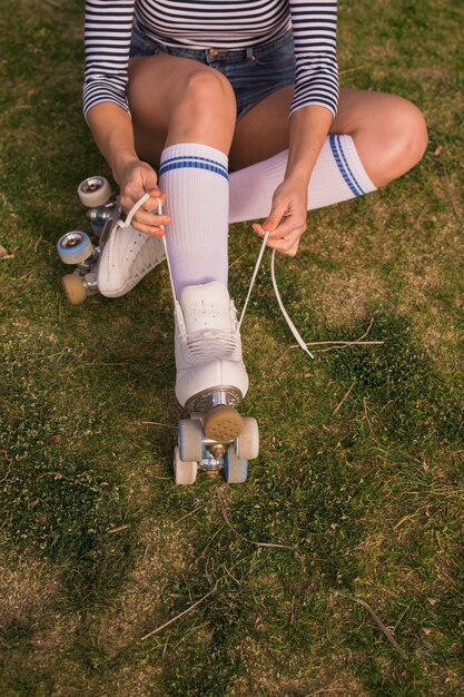 Foto gratuita una vista ambientale di un pattinatore femminile che lega il merletto del pattino di rullo che si siede sull'erba verde