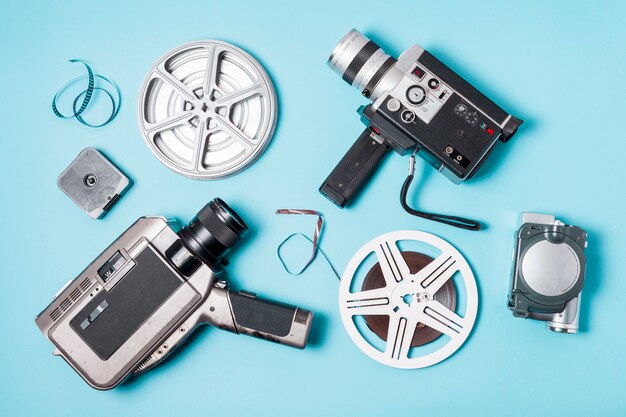 An overhead view of film strips; film reel and various type of camcorder on blue background