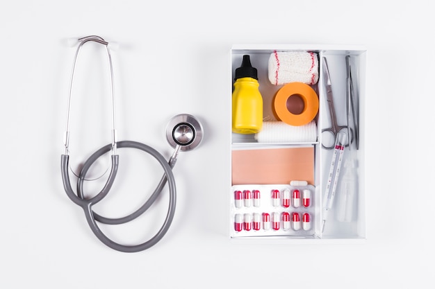 Overhead view of first aid kit and stethoscope on white background