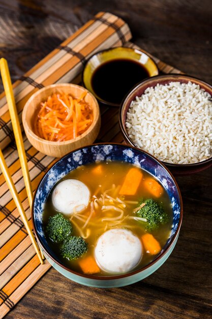 An overhead view of fish ball soup with rice and sauces on placemat