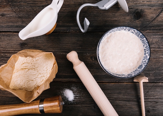 An overhead view of flour; milk; yeast and peppermill with rolling pin on table
