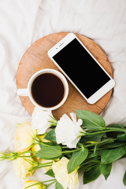 ベッド上のコーヒーカップと携帯電話と花の花束のオーバーヘッドビュー