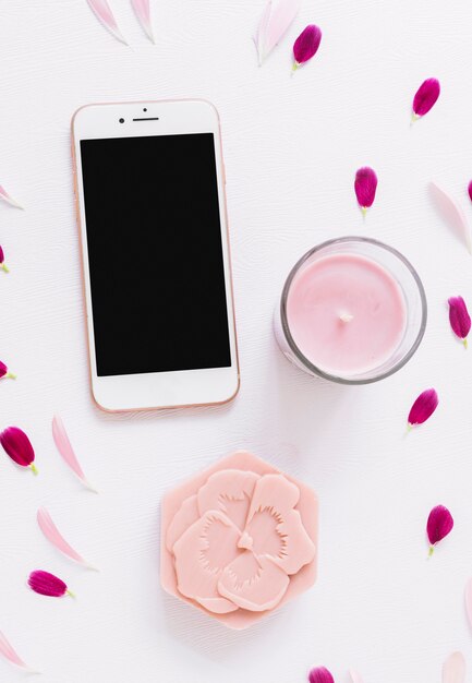 An overhead view of flower shape soap; candle and smartphone decorated with petals