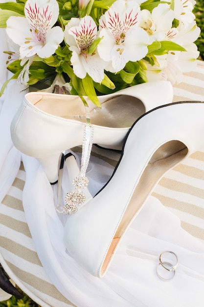 Free photo an overhead view of flowers; high heels; crown; scarf and wedding rings on table