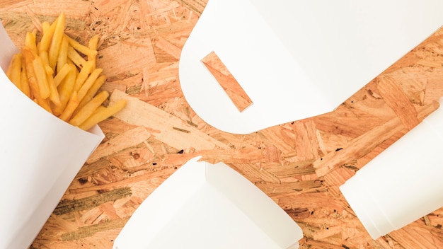 An overhead view of french fries and white package on wooden backdrop