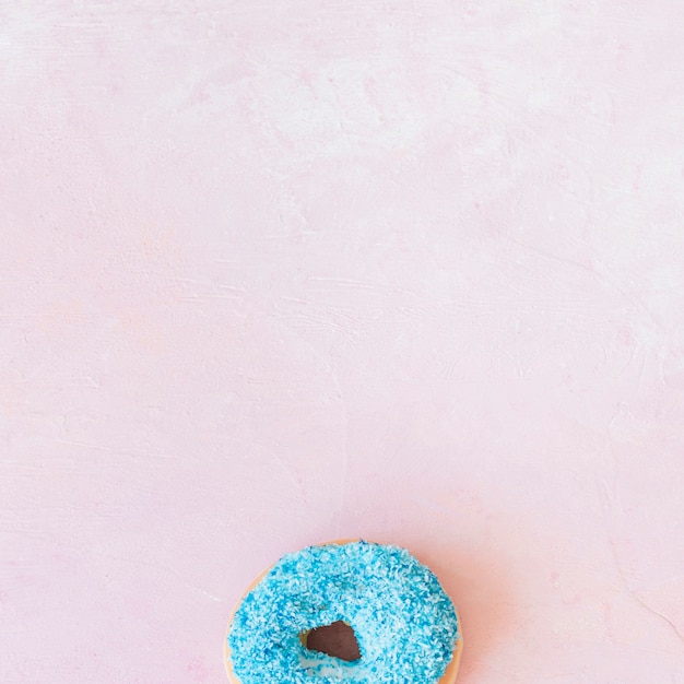 Overhead view of fresh blue donut at the bottom of pink backdrop