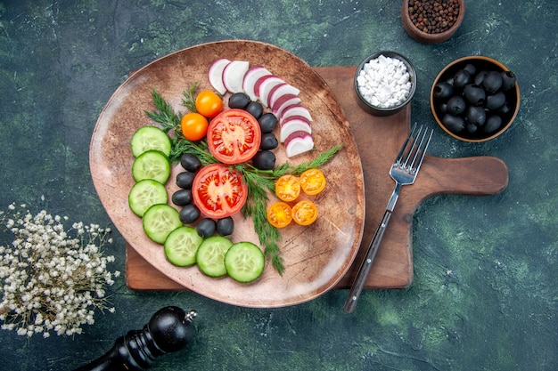 Overhead view of fresh chopped vegetables in a brown plate on wooden cutting board olives in bowl salt garlics flower on mixed colors background