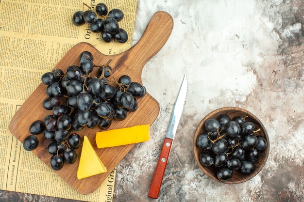 Вид сверху свежей вкусной грозди черного винограда и различных видов сыра на деревянной разделочной доске