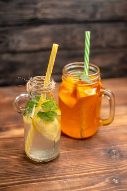 Overhead view of fresh detox water and fruit juice served with tubes on the left side on a brown background