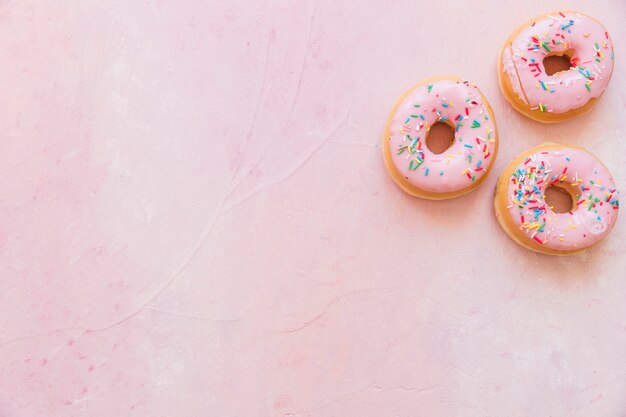 Верхний вид свежих пончиков с брызгами на розовом фоне