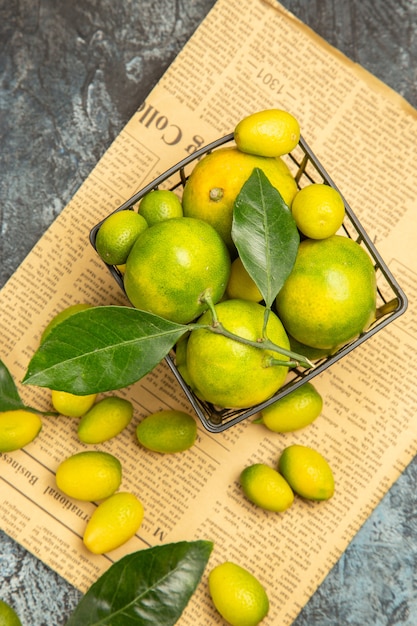 Overhead view of fresh kumquats and lemons in a black basket on newspapers on gray background stock image
