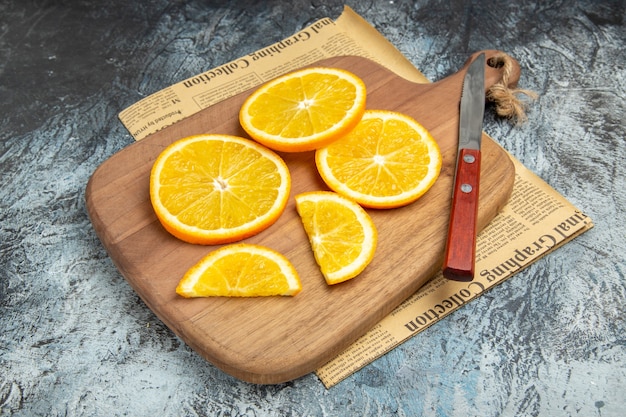 Foto gratuita vista dall'alto di fette di limone fresche con coltello su tagliere di legno su giornale su sfondo grigio