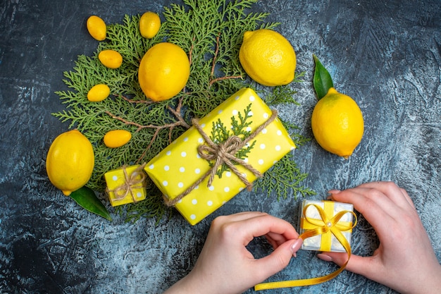 Overhead view of fresh lemons with leaves a plate with kumquats on fir branches hand opening a gift box on dark background