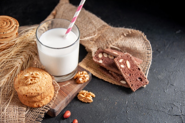 Overhead view of a fresh milk in a glass cookies spikes on nude color towel walnuts peanuts on the right side on dark background