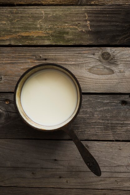 Верхний вид свежего молока в старой кастрюле над деревянным столом