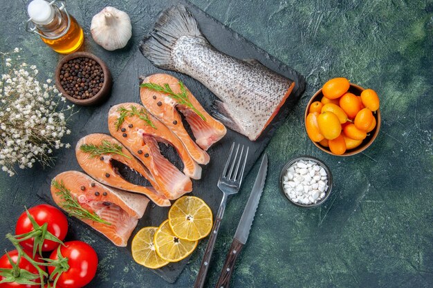 Overhead view of fresh raw fishes greens pepper and lemon slices on dark color tray oil bottle vegetables on mix colors table