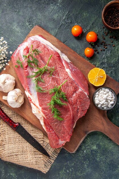 新鮮な生の赤身の肉の俯瞰図緑のニンニクレモン塩茶色の木製まな板ナイフヌードカラータオルトマトコショウ暗い色の背景