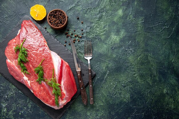 Overhead view of fresh red raw meat green on cutting board and pepper lemon cutlery set on the right side on green black mix color background