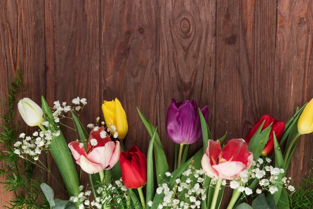 An overhead view of fresh tulips and baby's breath flower on wooden desk