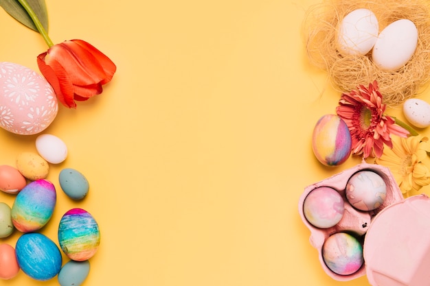 Free photo an overhead view of fresh tulips; gerbera and colorful easter eggs on yellow surface