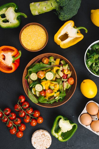 An overhead view of fresh vegetable salad; eggs; puffed rice cake and polenta on black concrete backdrop