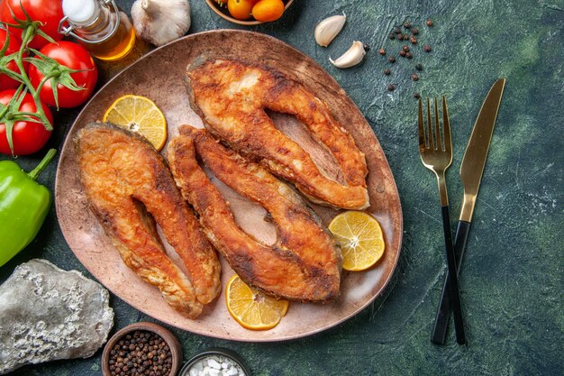 Overhead view of fried fishes and lemon slices on a brown plate spices tomatoes oil bottle on mix colors table with free space