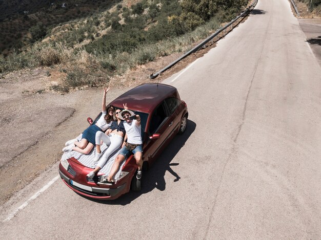 Overhead view of friends sitting on car hood taking self portrait