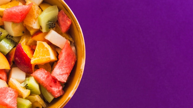 An overhead view of fruit salad in bowl against purple background