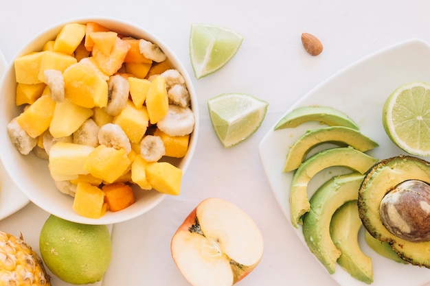 An overhead view of fruit salad bowl and avocado slices on white background